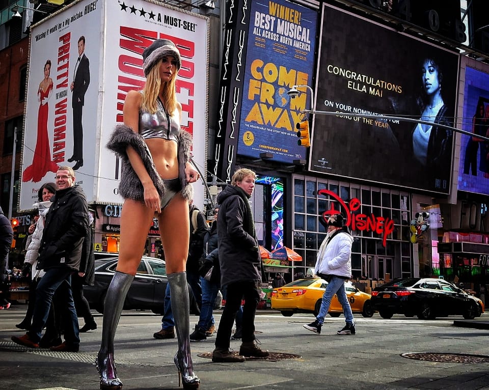 A giant advertising panel with a model above an evening street, a flow of people and taxis beneath