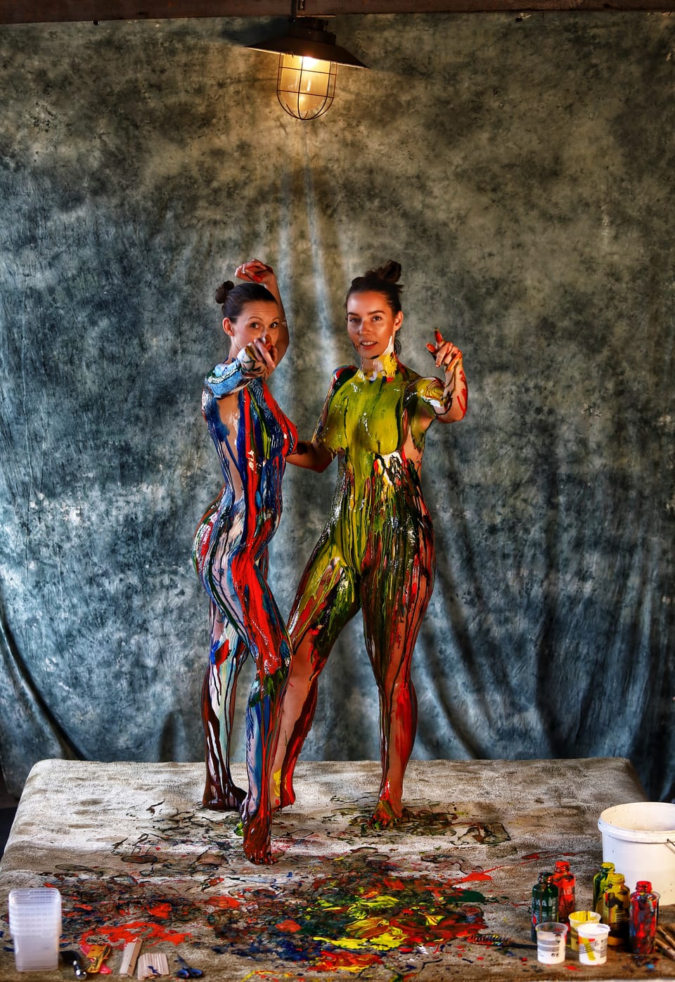 Body-painted models posing before a painted backdrop, spilled colour at their feet