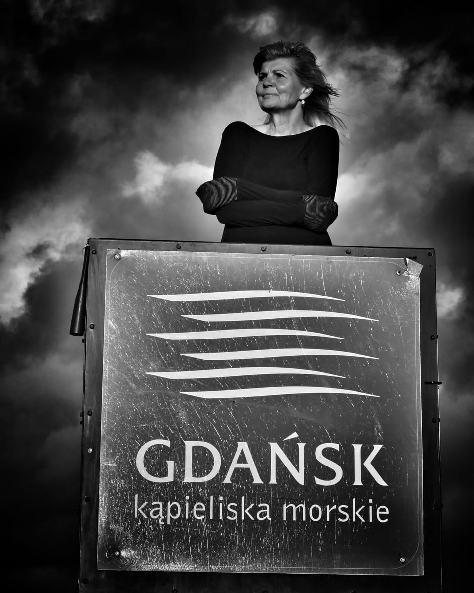 A woman standing behind an enamel sea-baths sign under a storm sky