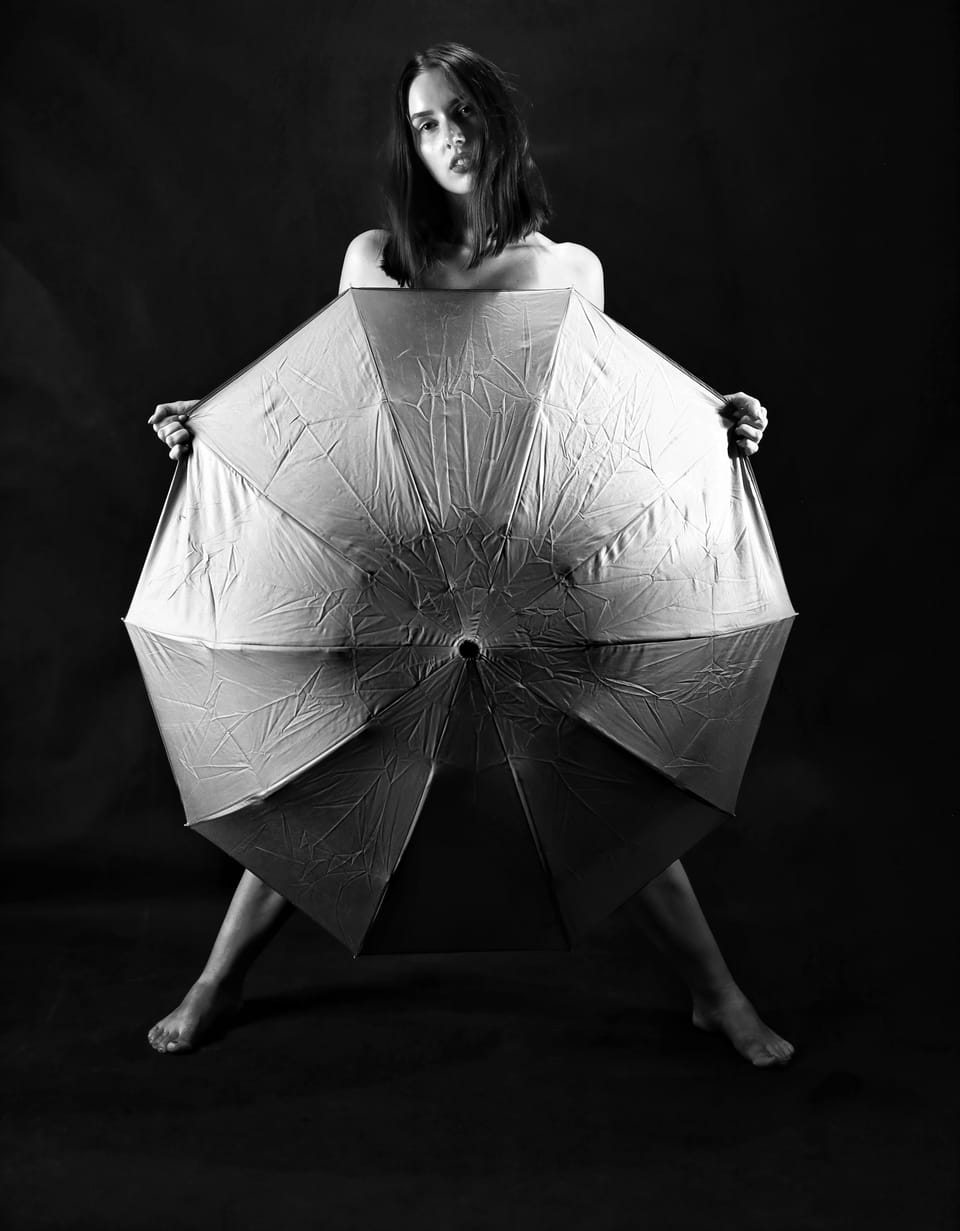A woman holding an open umbrella before her body, only bare feet showing