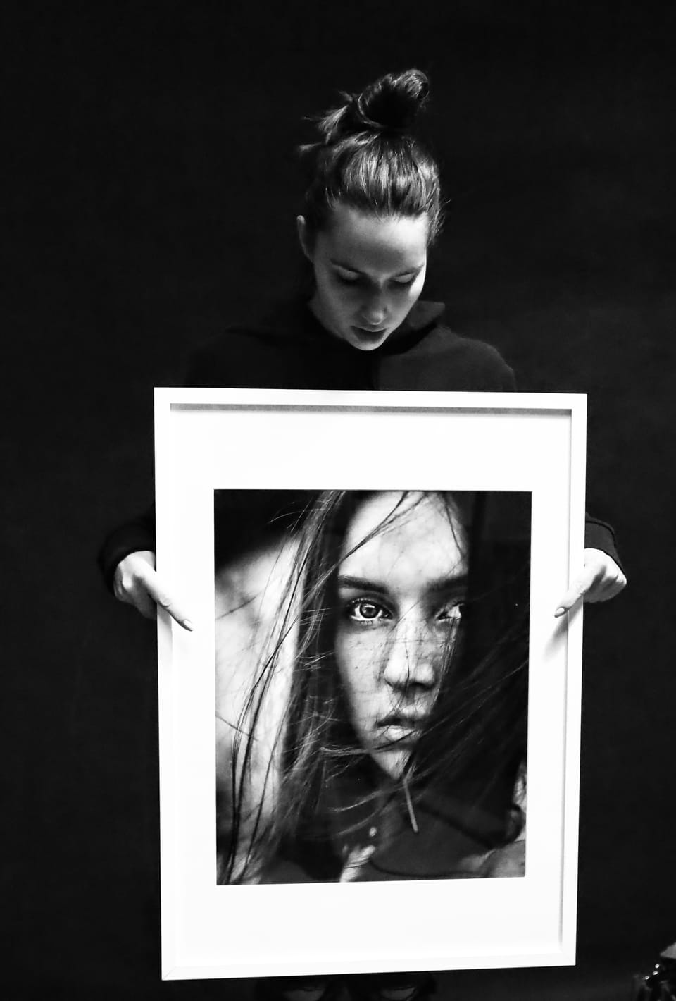 A woman holding a framed portrait before her, and the portrait is her again