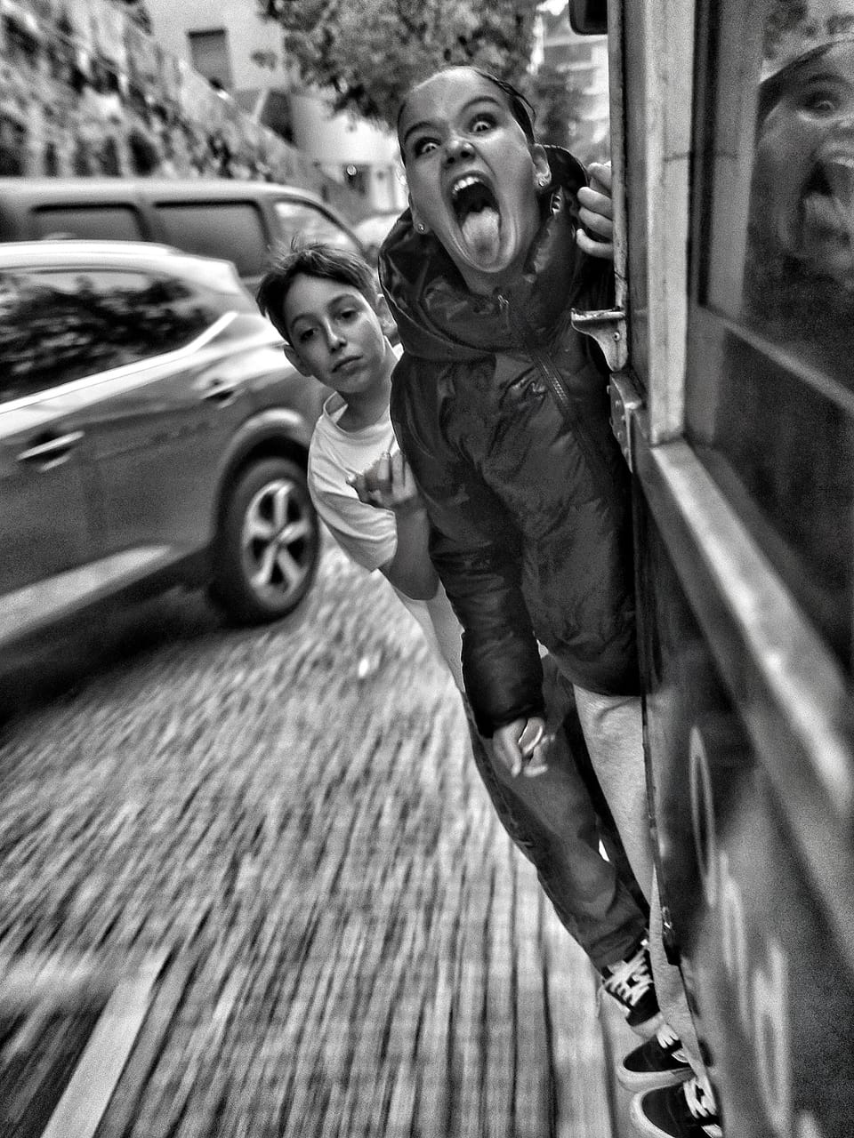 A girl in the street sticking her tongue out at the lens, the city blurred around her