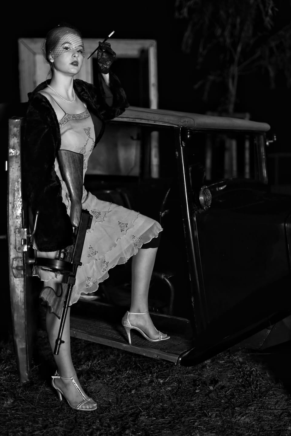 A woman in a fur coat and lingerie beside an old farm machine in a barn