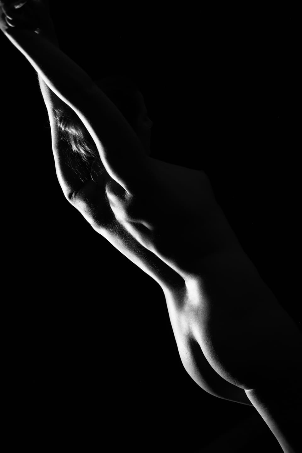 A nude study in deep shadow, light tracing only the line of an arm and hip