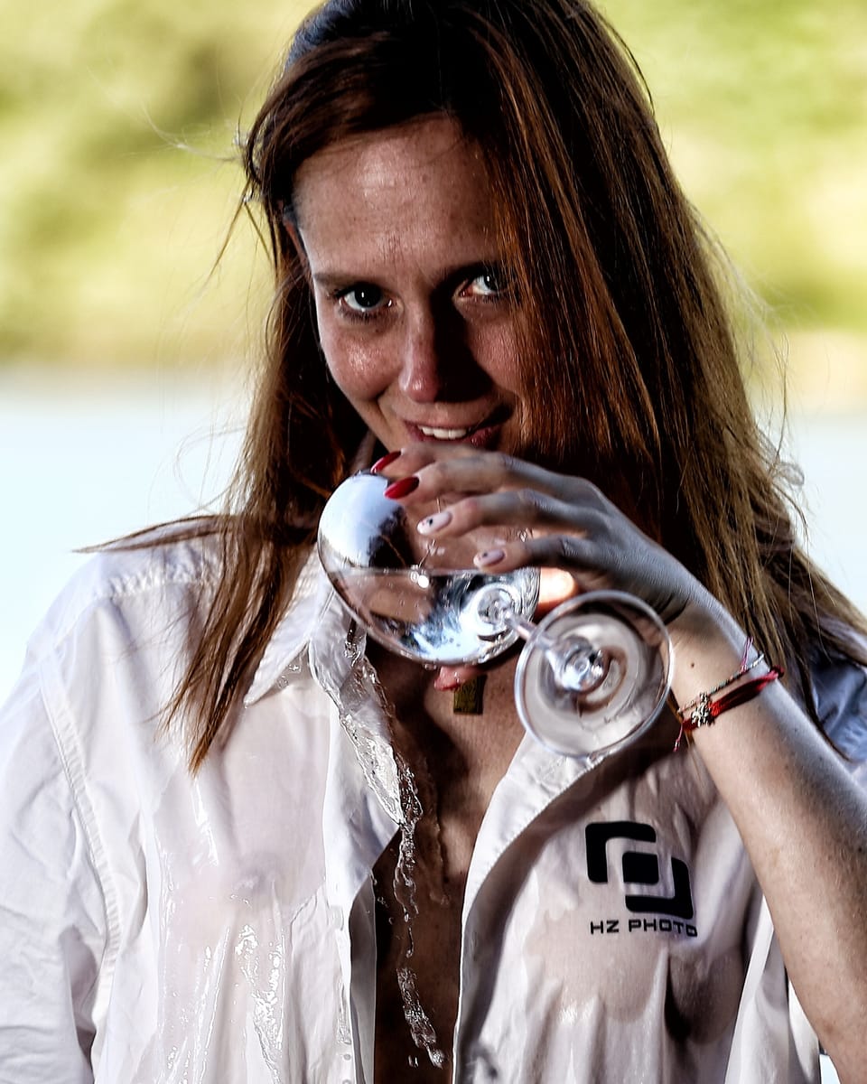 A woman in a soaked shirt drinking from a glass, water running down the fabric