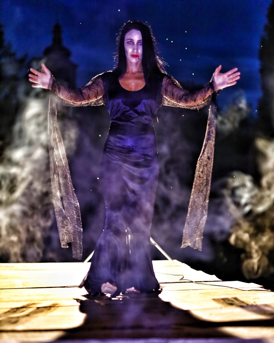 A model in a long gown at the end of the runway, arms wide in violet smoke