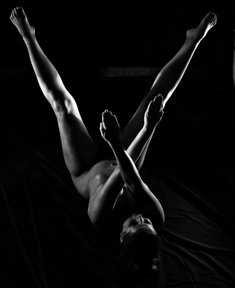 Legs raised into black space, the body below only suggested by light