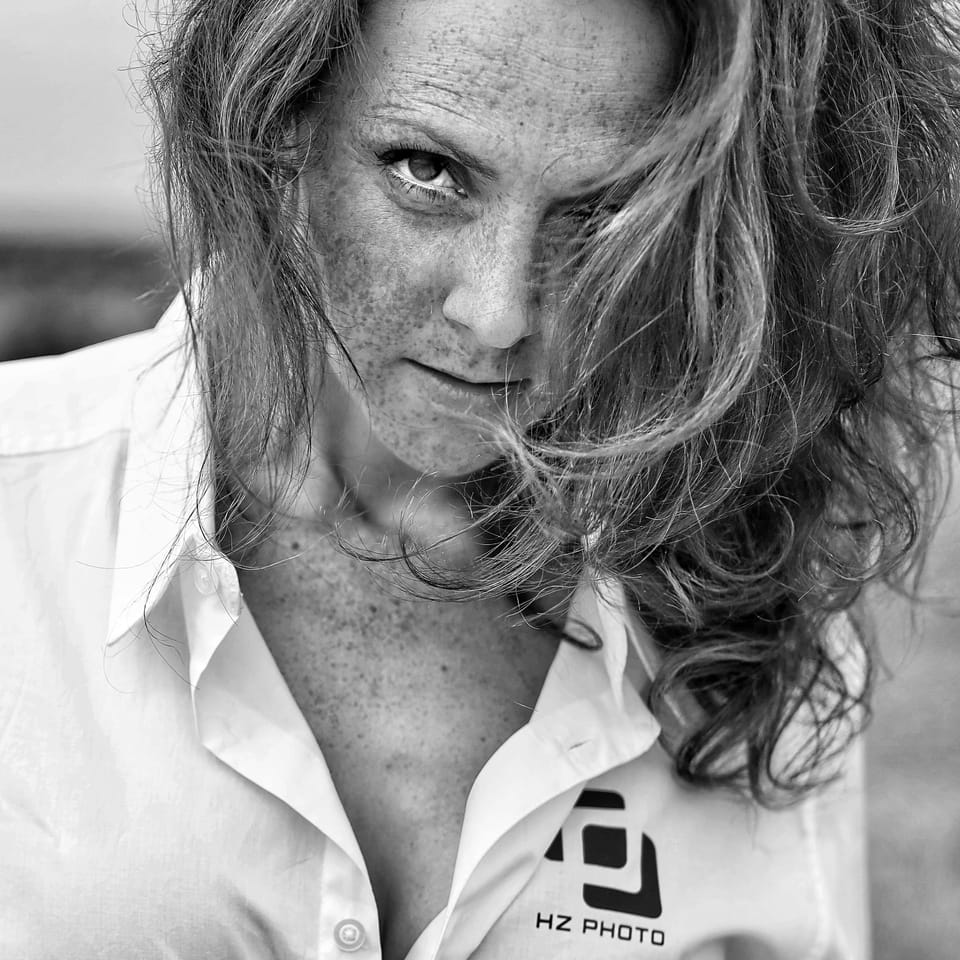 A close portrait of a freckled woman with wind-blown hair in an open shirt