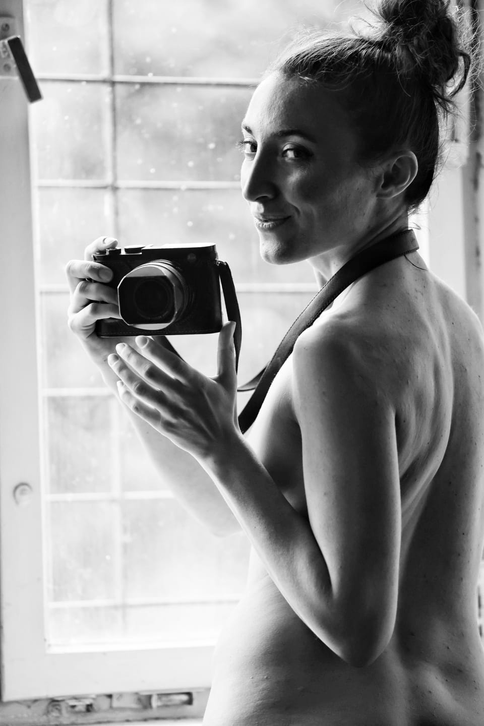 The model holds a camera and turns it back toward the window, the roles briefly reversed