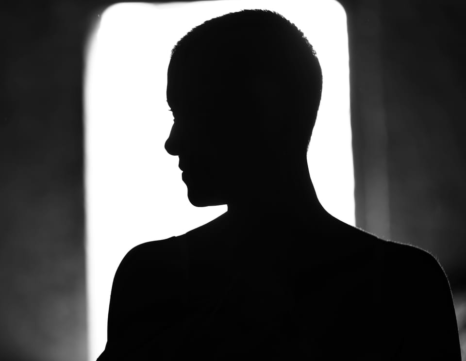 The silhouette of head and shoulders against a lit window, the face kept hidden