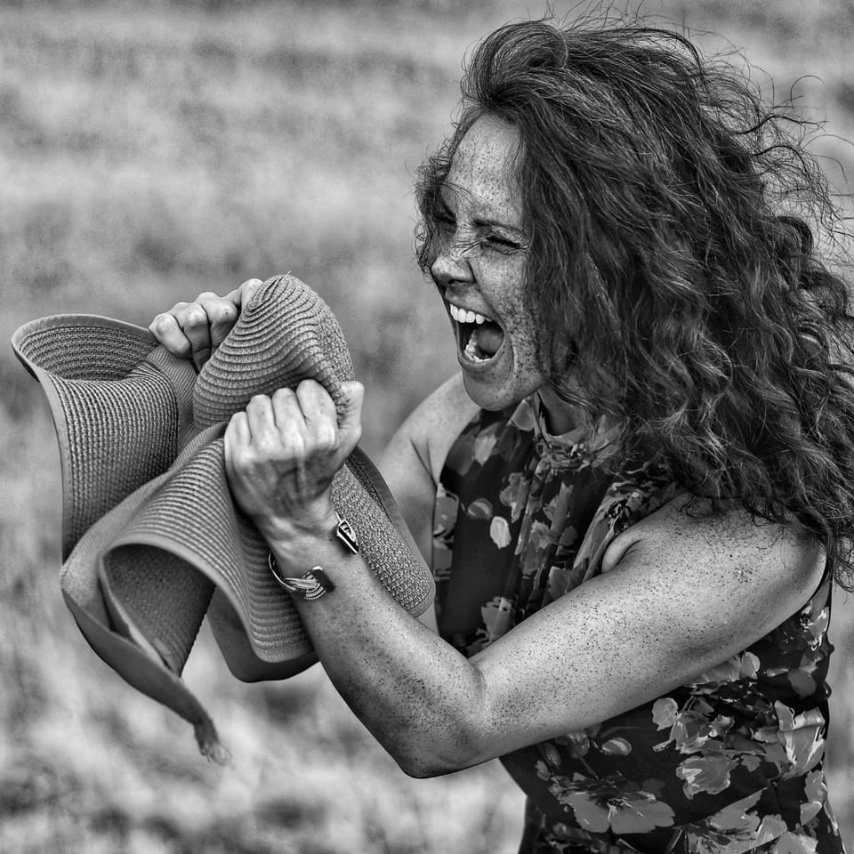 A laughing woman clutching a rolled fabric, curly hair thrown out to the sides