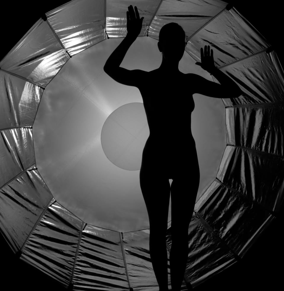 A second frame in the ring of light, palms braced against the inner rim
