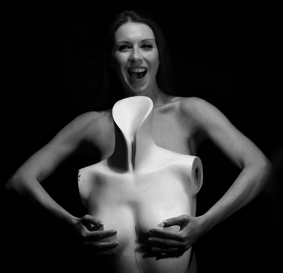 A laughing woman holding a white sculptural torso in front of her body