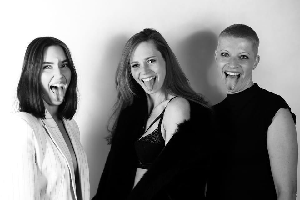 Three women side by side with their tongues out, plain studio light