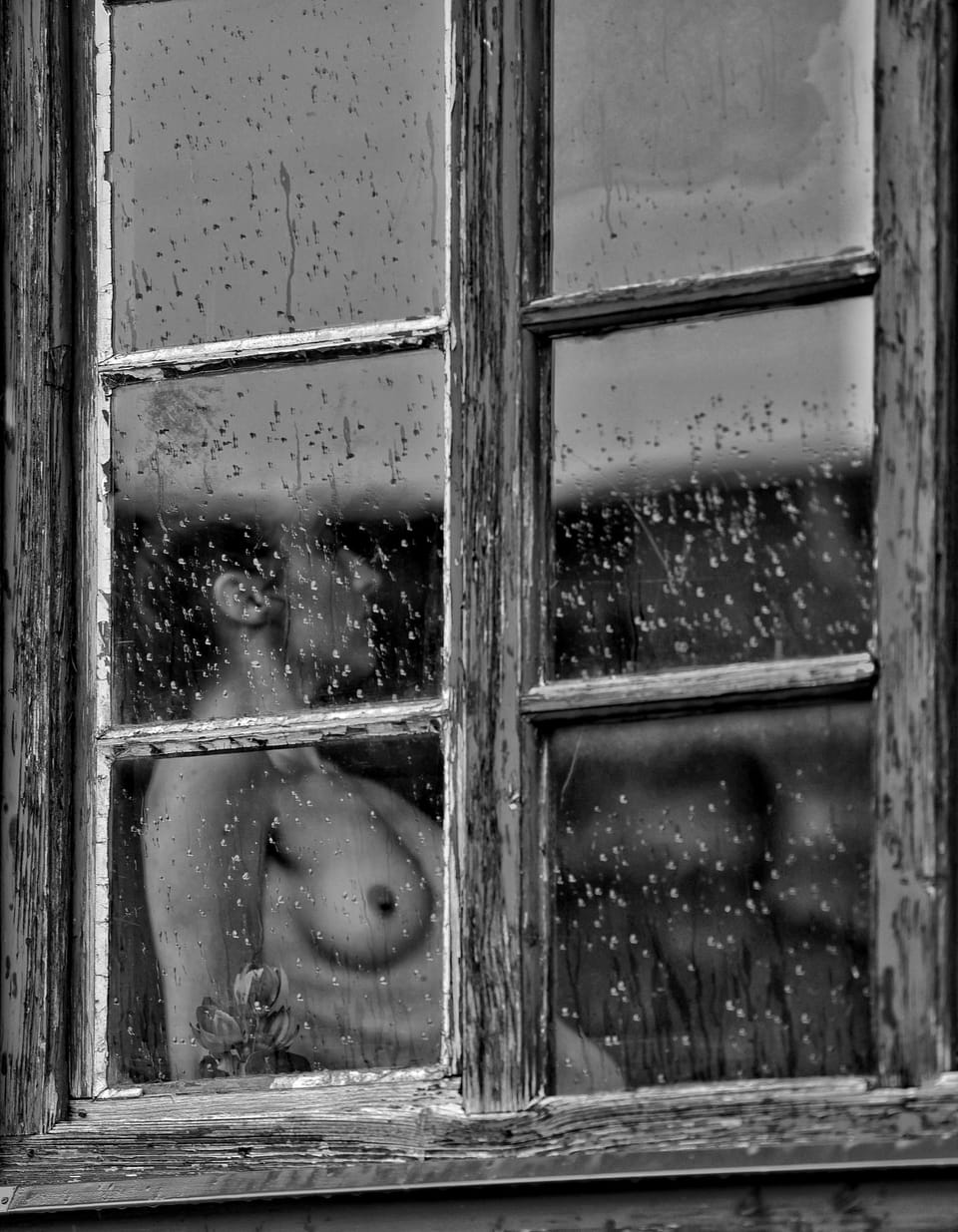 A figure behind an old rain-spotted window, the glass dividing the body into panes