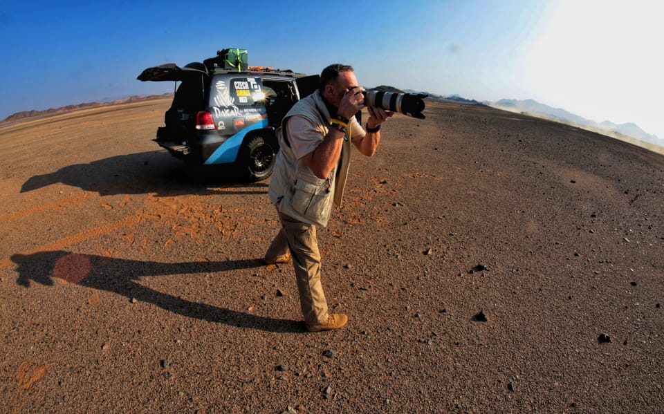 Zbyněk Hozák shooting with a long lens in the desert, the support vehicle behind him