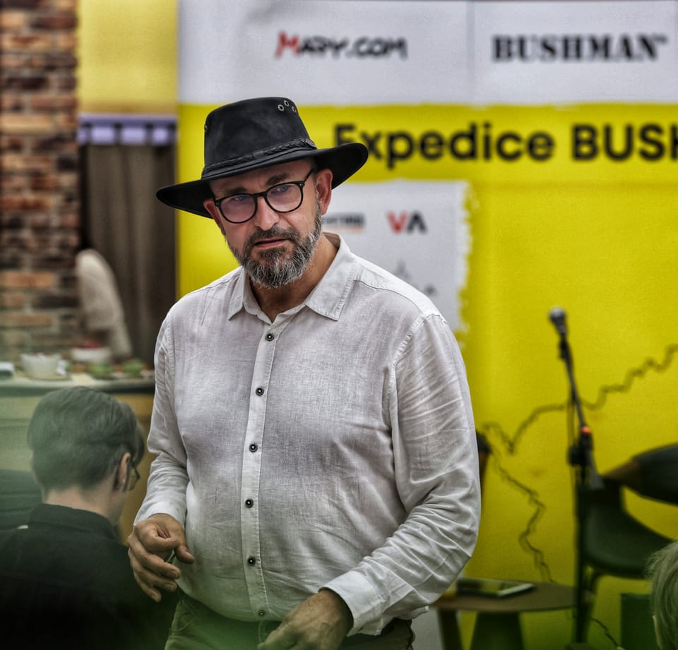 A man in a black hat before the yellow backdrop of an expedition talk