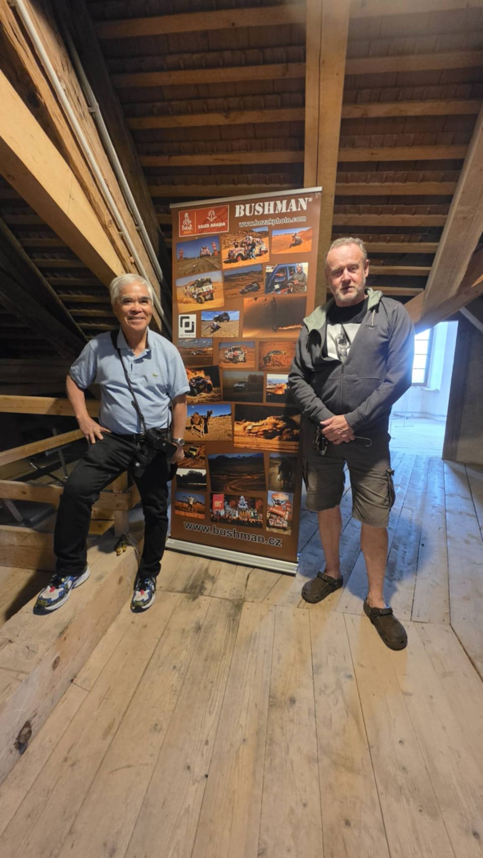 Two men beside a roll-up banner in a loft with a plank floor