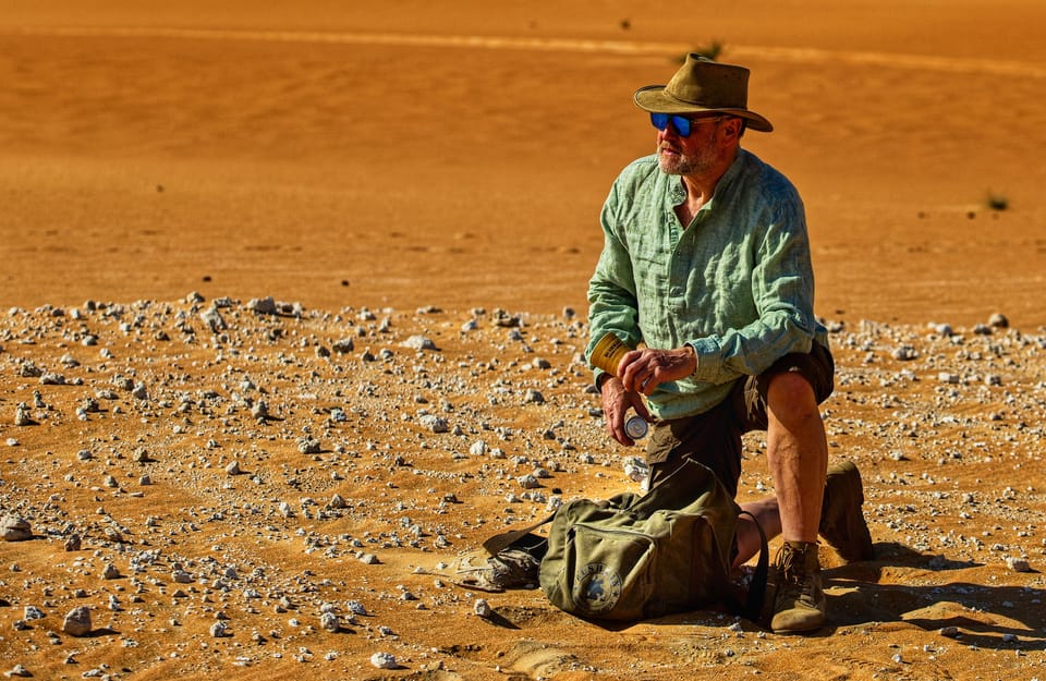 A man kneeling on stony flats sorting his kit, the desert running out into nothing
