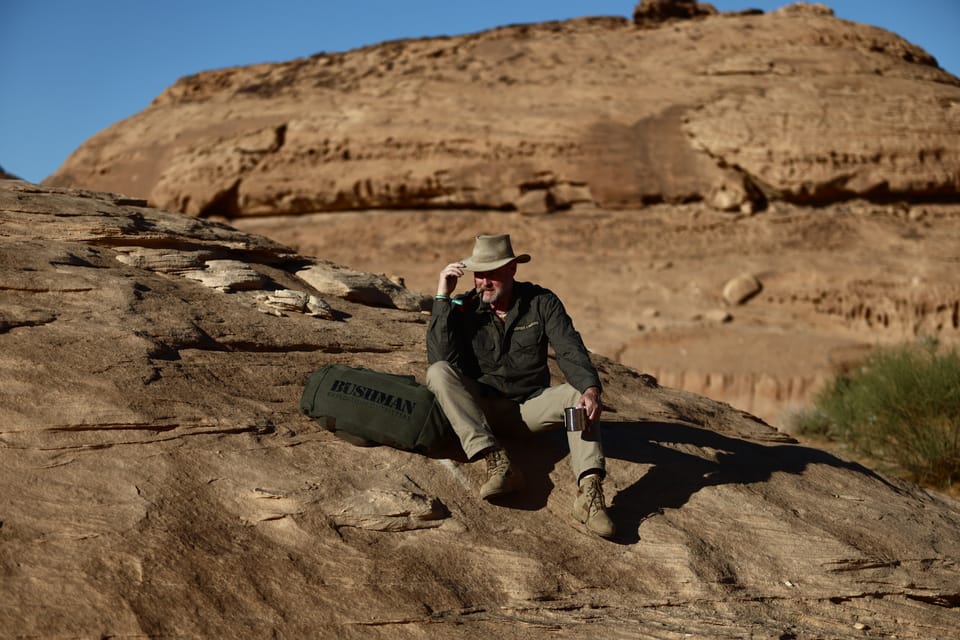A man on the rock straightening his hat, layered sandstone walls behind him