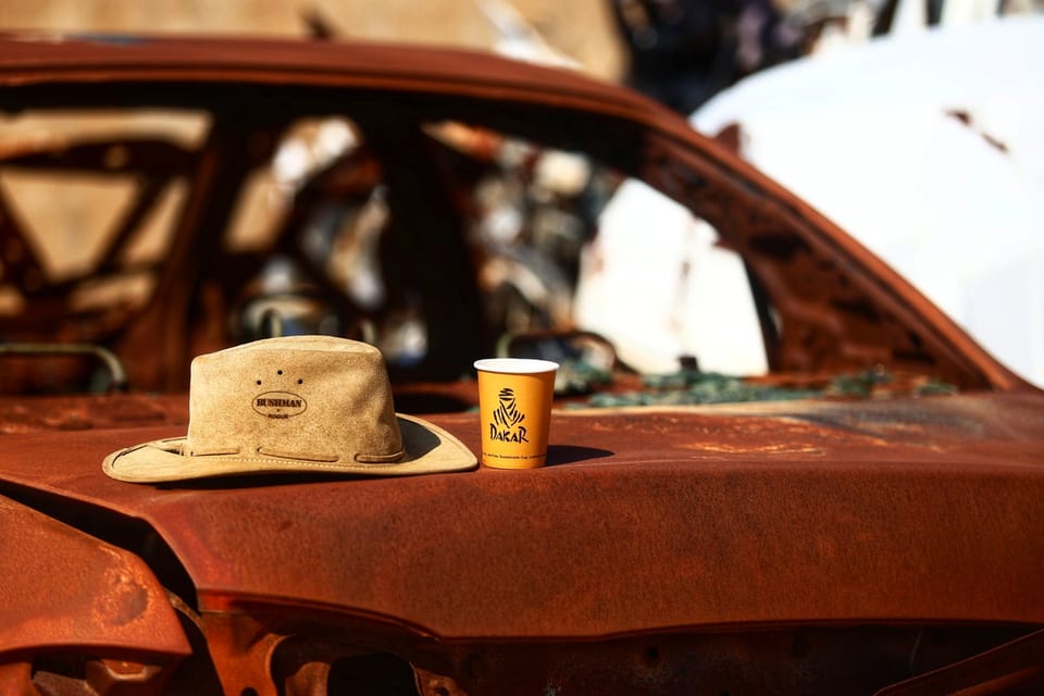 A hat and a paper cup left on the bonnet of a rusted wreck