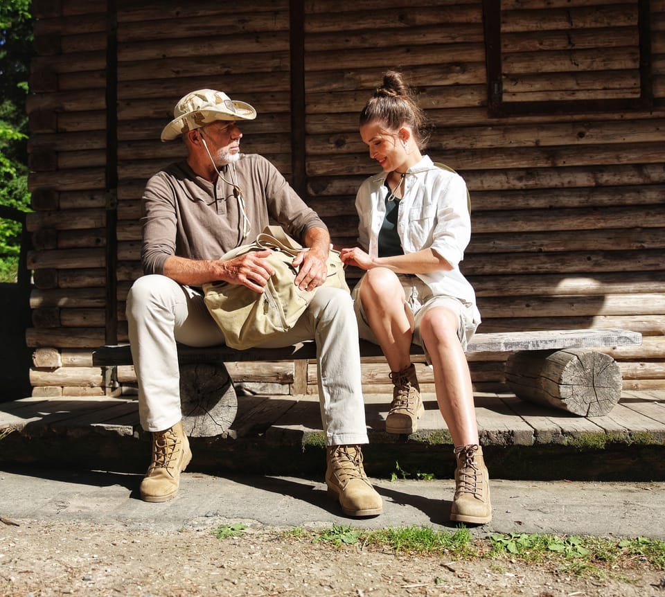 Two people on a bench before a log wall, midday without shadow