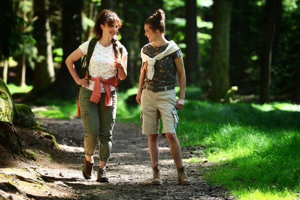 Two women with backpacks walking a sunlit forest path