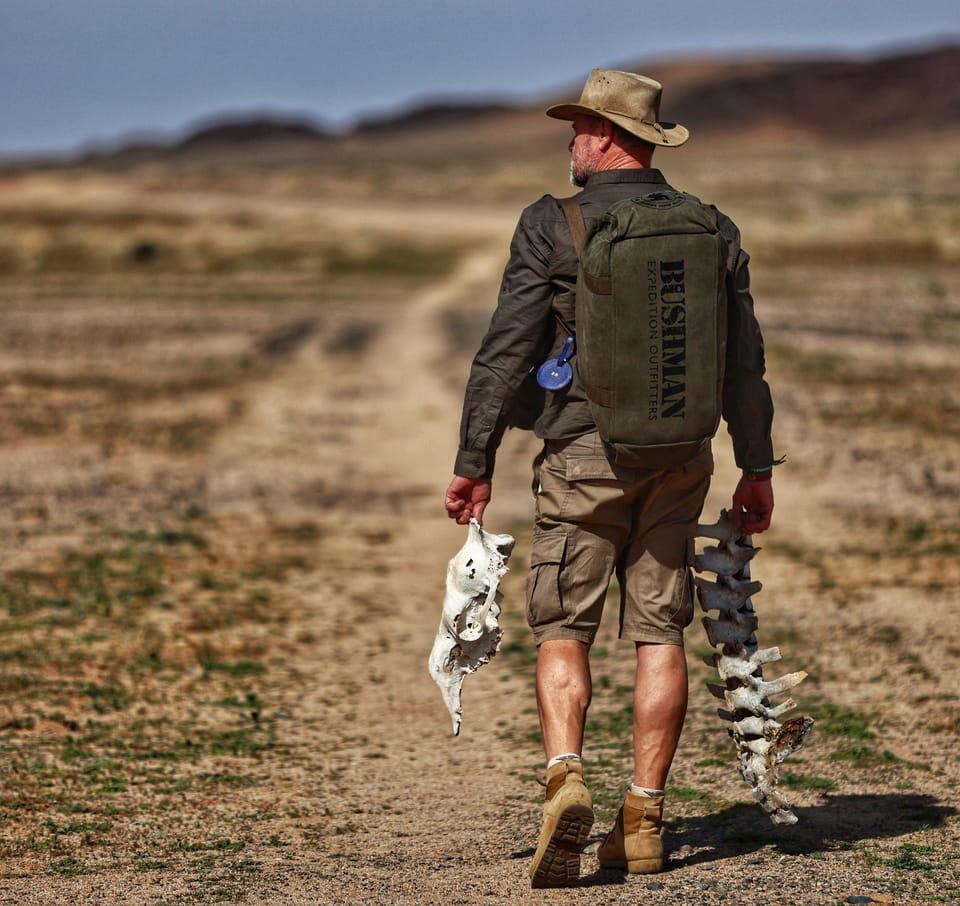 A man with a backpack returning along a dusty track, a fish in each hand