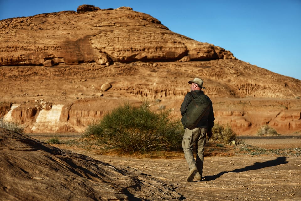 A figure with a backpack walking away across the desert plain below a rock massif