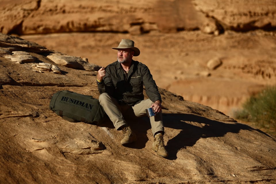 A break on a rock outcrop in the middle of the desert, a duffel lying beside him