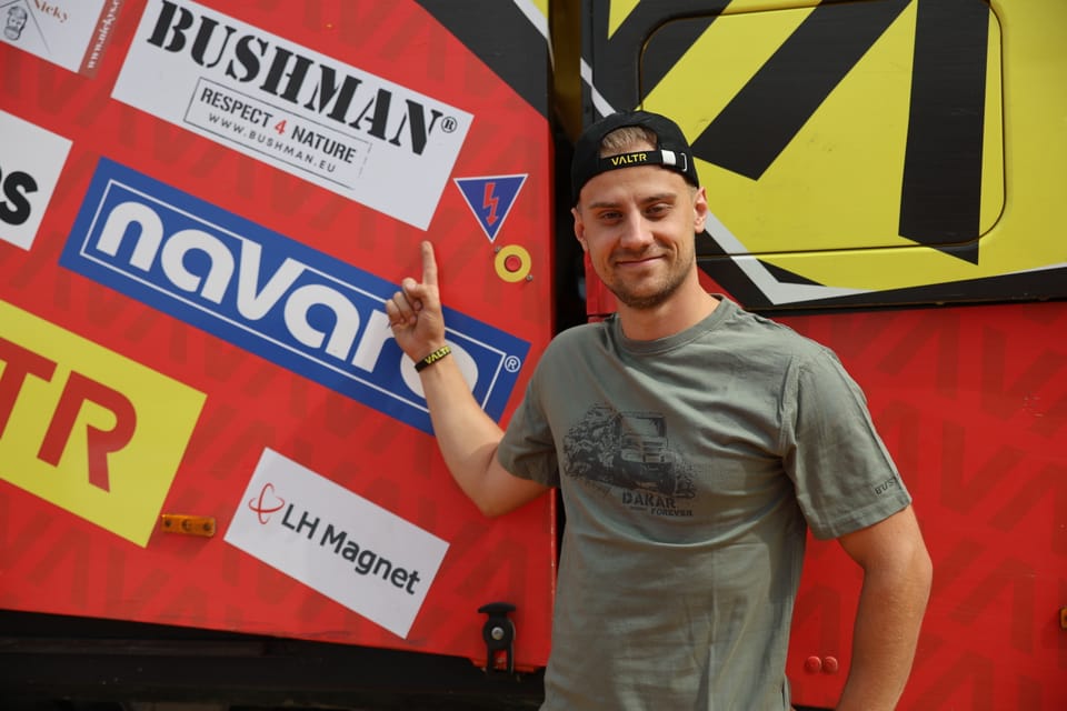 A young man giving a thumbs-up beside a race car covered in partner decals