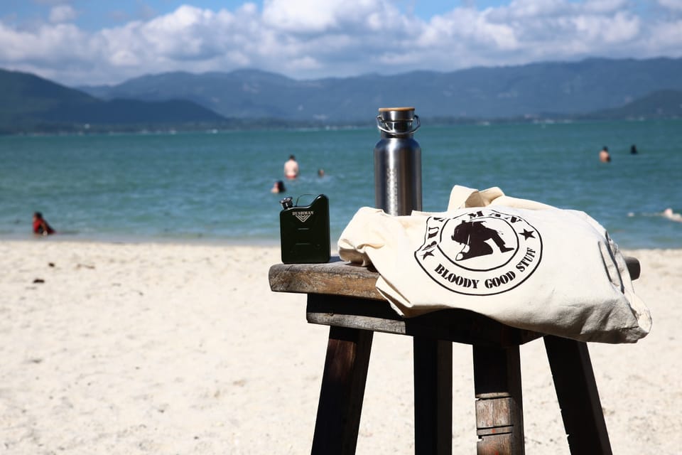 A canvas bag and a bottle on a stool on the beach, the sea and hills behind