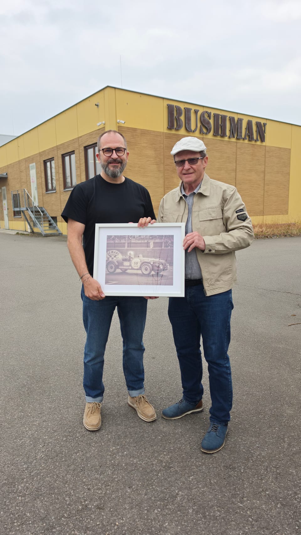 Two men holding a framed photograph in front of a building bearing the company name