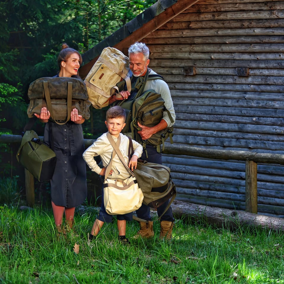 A family with duffels posing at a wooden wall on the forest edge