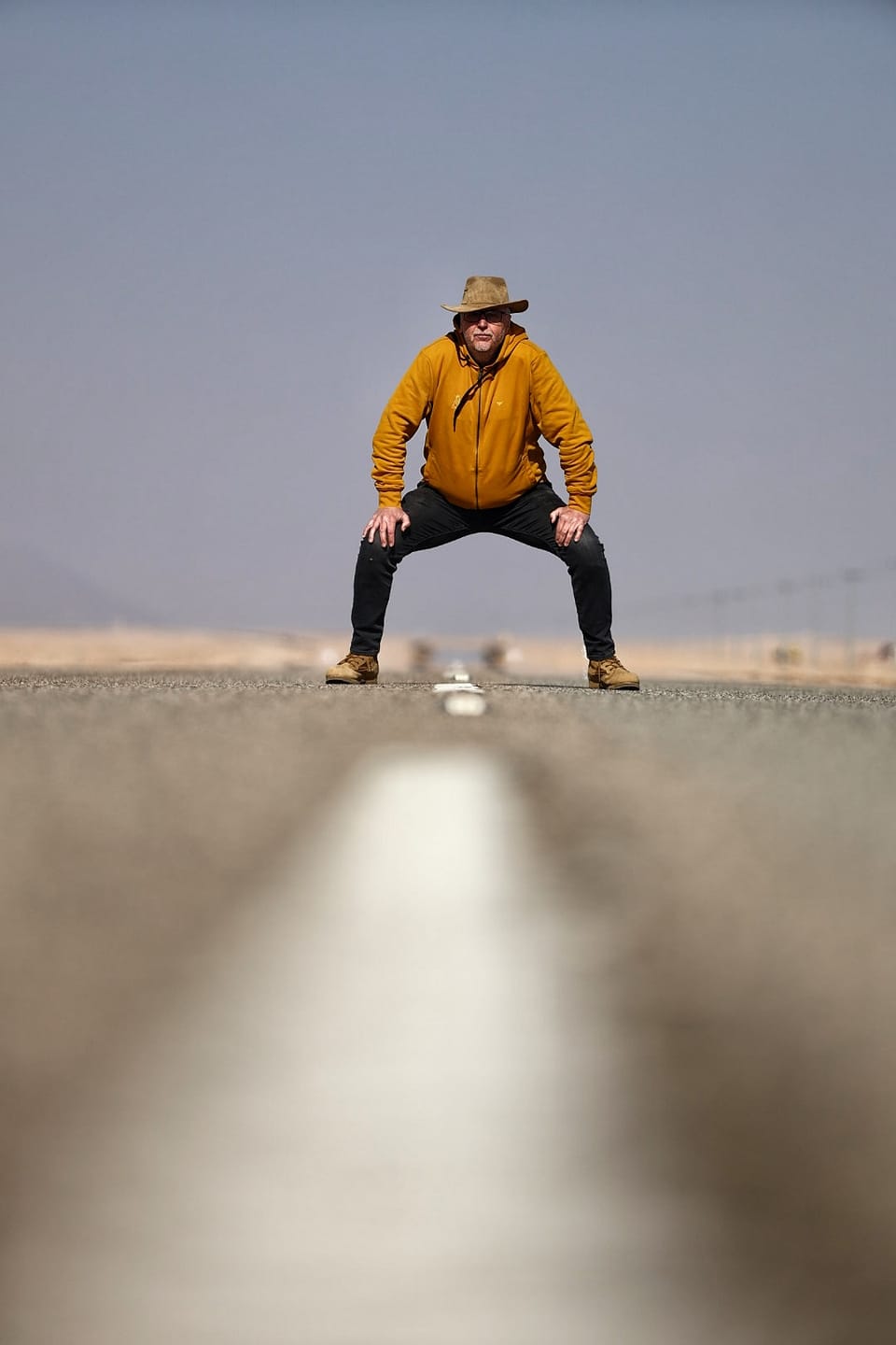 A figure standing astride the centre line of a road that vanishes into heat haze