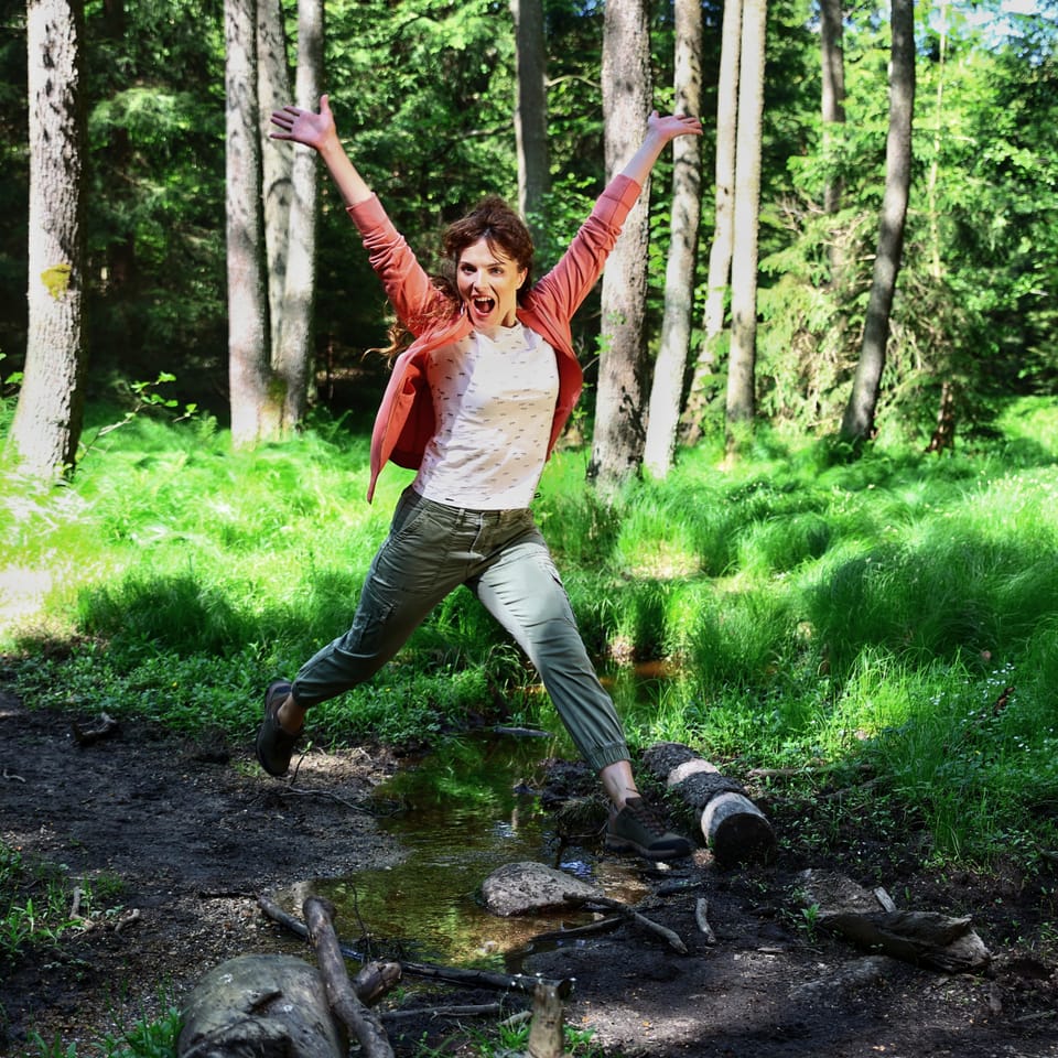 A woman leaping with arms wide in a light-filled forest