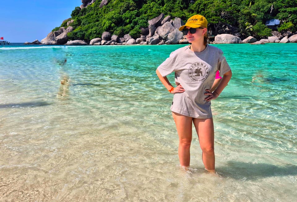 A woman in a T-shirt standing knee-deep in turquoise water by a rocky island