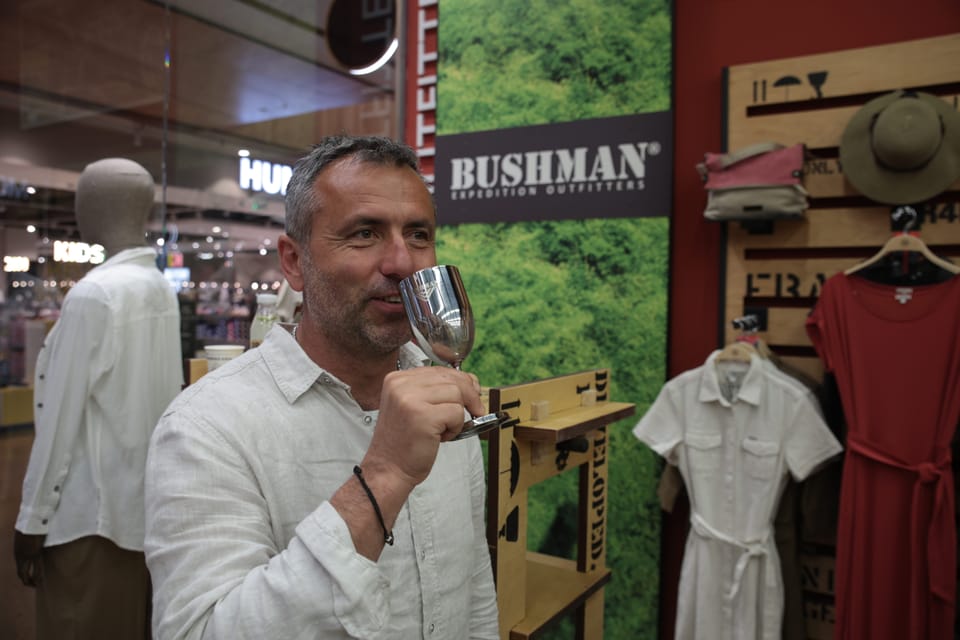A man drinking from a tin mug in the middle of a shop floor of display racks