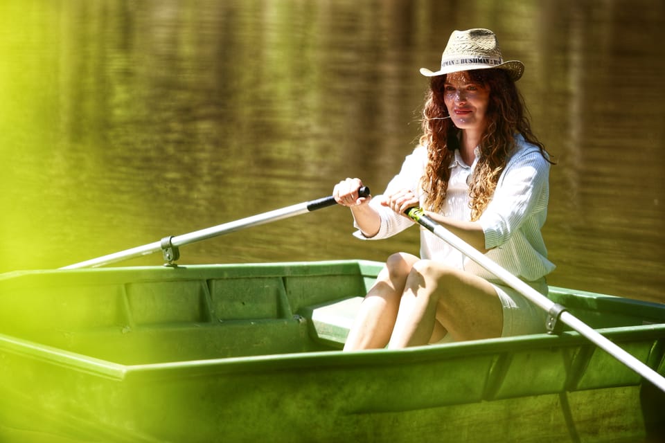 A woman in a straw hat rowing across the green surface of a pond