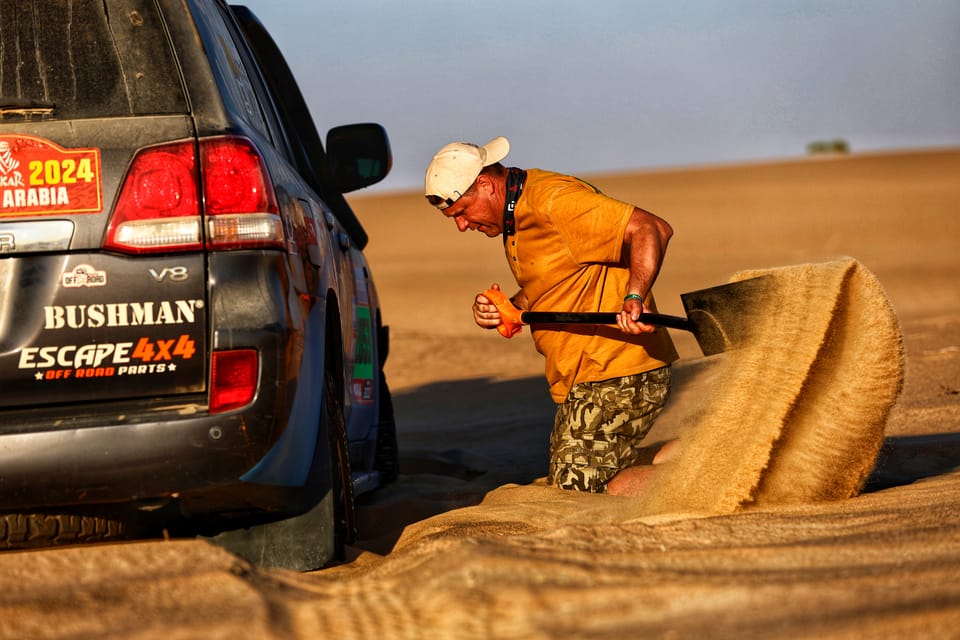 A man pulling a sand ladder from under the tail of a 4x4 bogged in the sand