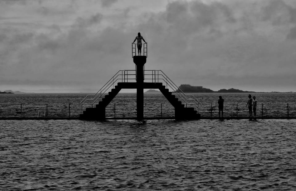 A black and white landscape, a diving tower on a sea pier under heavy cloud