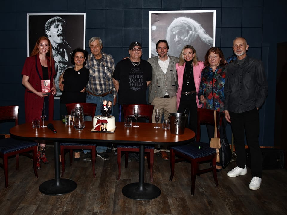 A group at a talk, large portraits on the wall, glasses on the tables
