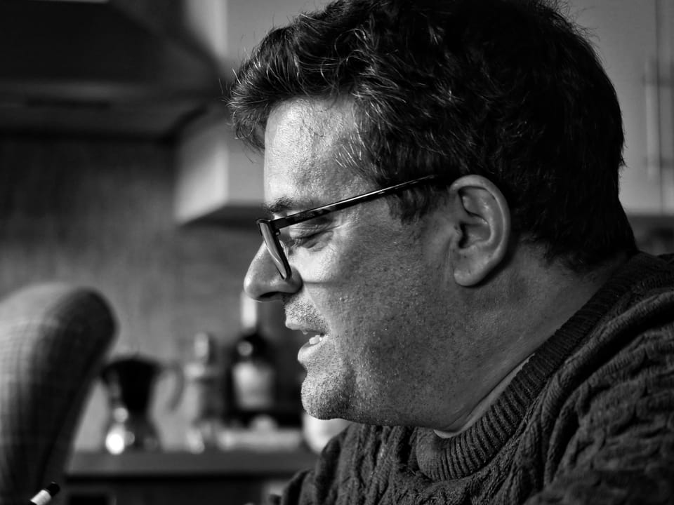A profile portrait of a man in glasses, the background dissolved to grey