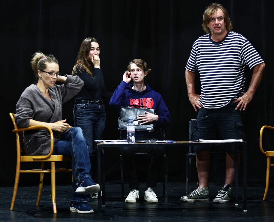 Four figures at a table on stage, one of them on the phone