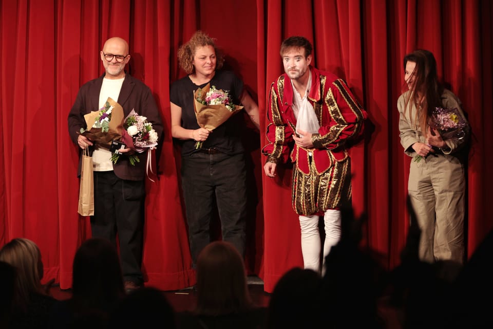 A curtain call before a red curtain, four company members holding bouquets