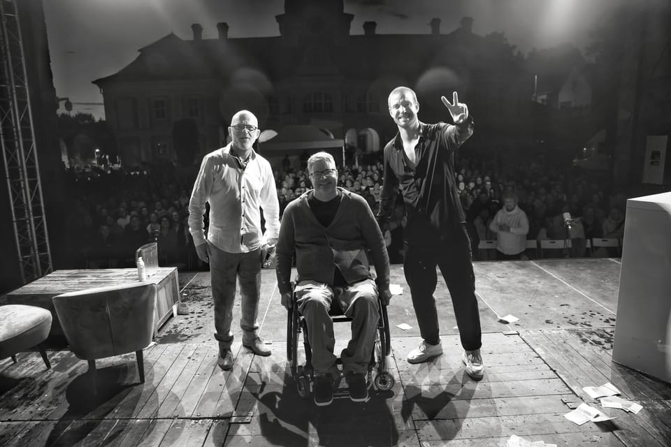 A curtain call before a full house, four on stage and one of them in a wheelchair