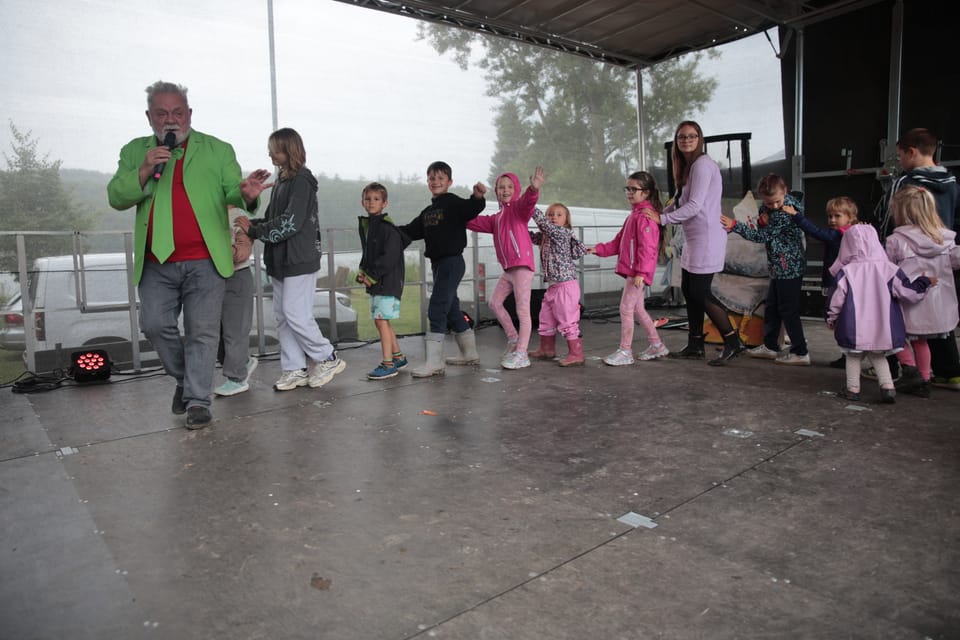 A man with a microphone leading a line of dancing children on an outdoor stage