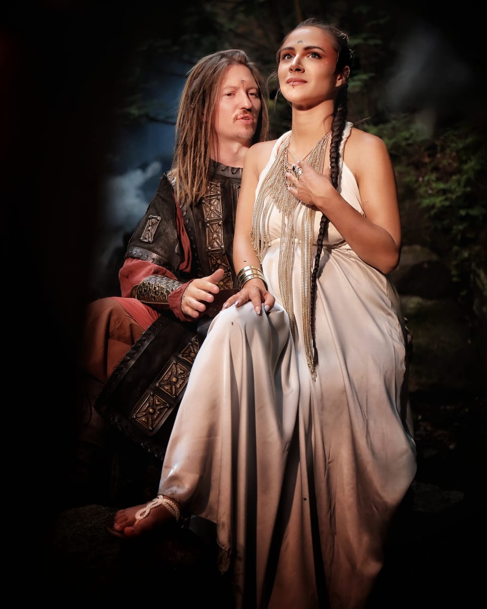 A pair in period costume before a painted forest backdrop