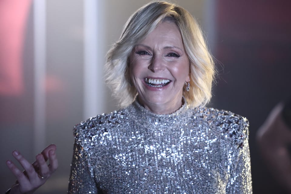 A woman in a silver sequinned jacket laughing, hands reaching toward someone out of frame
