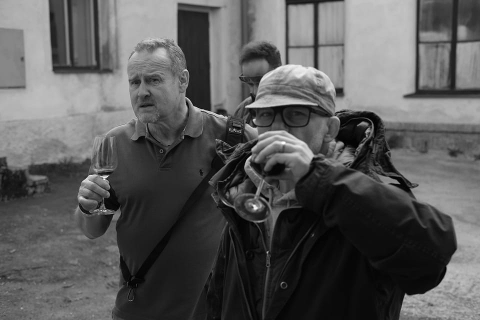 A photographer pressing the shutter, a man with a glass looking on beside him